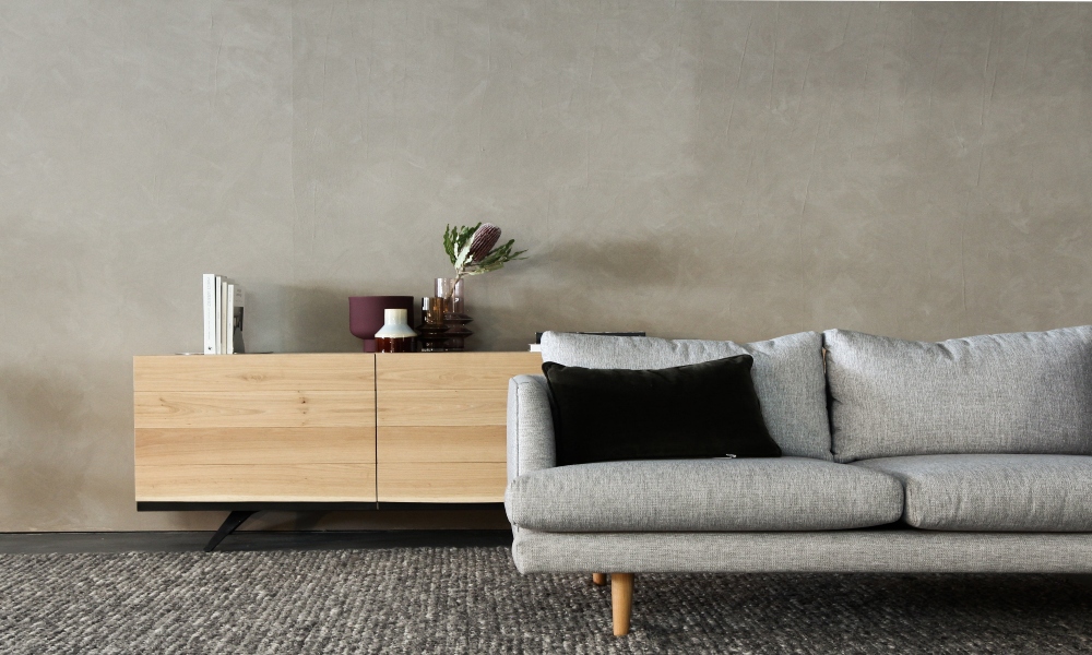 Grey sofa with black cushion, wooden table with books and plant